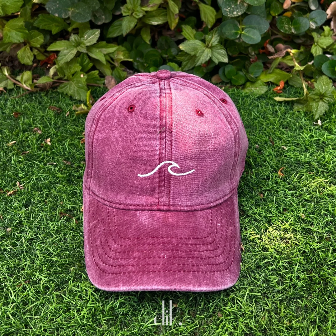 Pink cap with a white wave logo on grass
