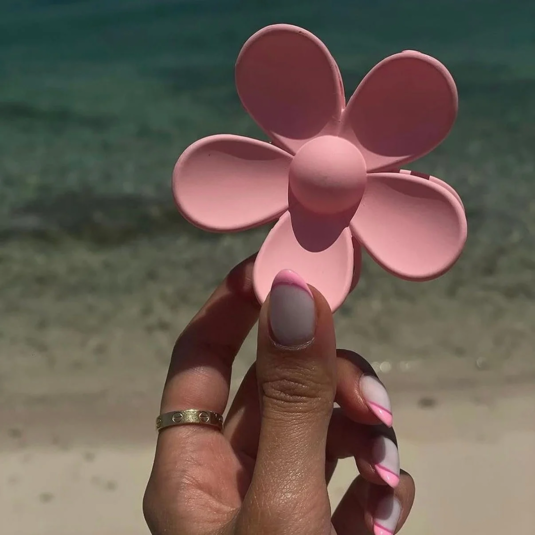 Hand holding a pink flower-shaped object with a blurred beach background